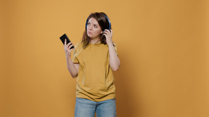 Woman using smartphone listening to music on wireless headphones and dancing stops to check sound. Confident person holding mobile phone using online streaming app for entertainment.