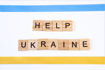 Top view phrase help ukraine is laid out of wooden squares isolated on white background. with flag of ukraine with blue and yellow ribbon. Concept of peace, war in Ukraine