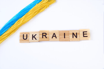 Top view phrase ukraine is laid out of wooden squares isolated on white background. with flag of ukraine with blue and yellow ribbon. Concept of peace, war in Ukraine