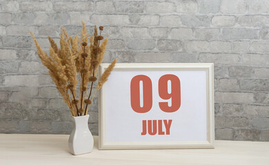 july 9. 9th day of month, calendar date. White vase with ikebana and photo frame with numbers on...