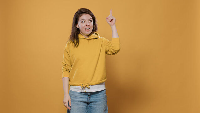 Portrait Of Smiling Woman Having An Idea Thinking Being Spontaneous Touching Temples With Index Finger Using Imagination In Studio. Casual Young Person Wearing Hoodie Having Inspiring Thoughts.