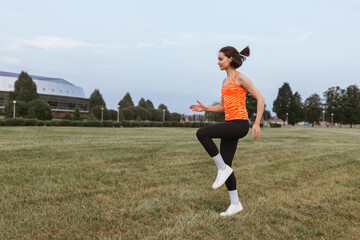 Sporty female runner running on spot on grassy meadow during cardio workout in summer 