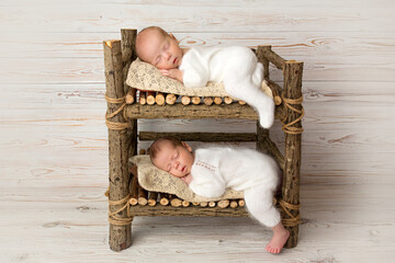 Tiny newborn twin boys in white bodysuits against a light wood background. Newborn twins sleep on a...