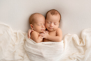 Tiny newborn twins boys in white cocoons on a white background. A newborn twin sleeps next to his brother. Newborn two twins boys hugging each other.Professional studio photography - obrazy, fototapety, plakaty