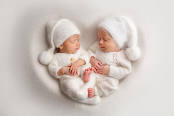 Tiny newborn twin boys in white bodysuits on a white background in white caps. Newborn twins sleep...