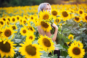 A beautiful young woman with bare shoulders smiles in a sunflower field. The theme of cosmetology,...