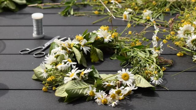 Homemade flower crown, or flower wreath, on the outdoor table. Flower crown made using wild flowers, wire and scissor. Traditional beauty and hair accessory for Midsummer celebration in Sweden.