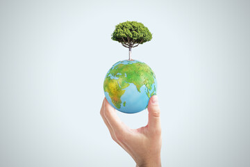 Close up of female hand holding abstract globe with tree on light background. World, earth, ecology and planet concept.