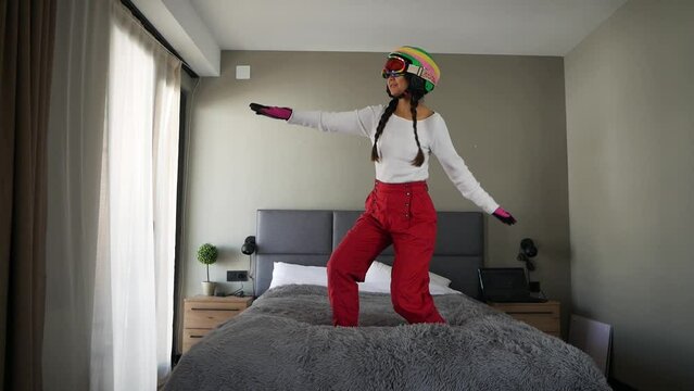 Funny asian girl snowboarder slide on bed in bedroom at home dreaming of trip to ski resort during lockdown due to coronavirus.
