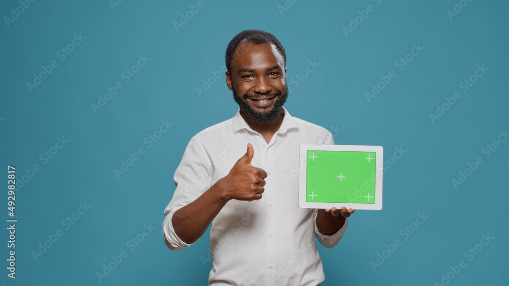 Poster happy man pointing at digital tablet with horizontal green screen in hand, showng isolated copy spac