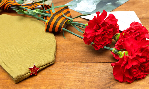 9th May. Postcard for the Victory Day. On a wooden background, a cap, a photo, carnations, a St. George ribbon. Memory of the Great Patriotic War. Soft Focus. Flat.