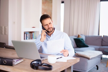 Confident man using laptop and mobile phone while working from home
