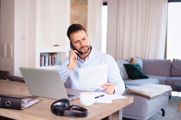 Confident man using laptop and mobile phone while working from home