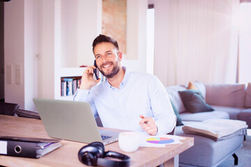 Confident man using laptop and mobile phone while working from home
