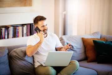 Happy man using mobile phone and laptop while relaxing at home