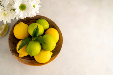 Bowl with fresh limes and lemons, on wooden background. Fresh citrus fruits with fresh flowers, copy space