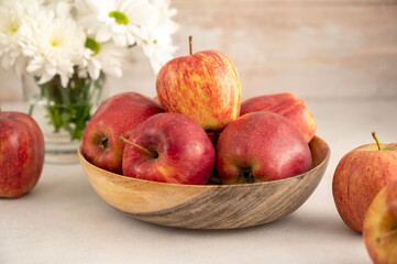 Red apples in bowl on wooden rustic background. Fresh red apple fruits with flowers.