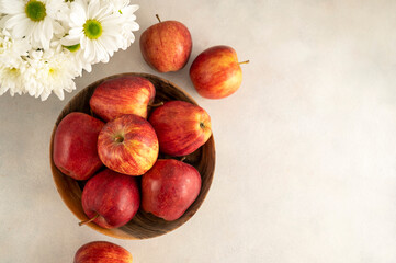 Red apples in bowl on wooden rustic background. Fresh red apple fruits with flowers, top view