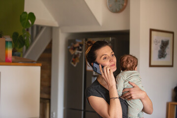 New Mum on phone looking worried whilst holding newborn