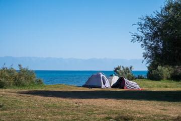 Tourists tents on Issyk-kol lake wild beach. Travel, tourism, recreation in Kyrgyzstan concept. Summer vacation.