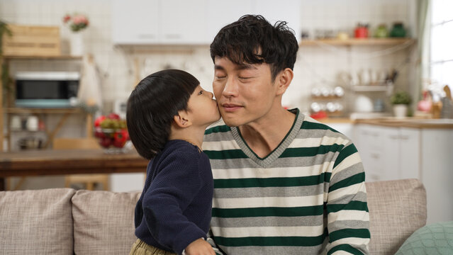 Asian baby boy feeling shy after kissing dad on face in the living room at home. happy family concept