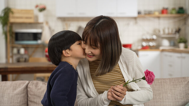 cute Asian boy giving a kiss on face and carnation flower to his mon on mother's day.