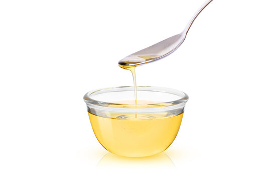 Cooking oil dripping from metal spoon into glass bowl isolated on white background.