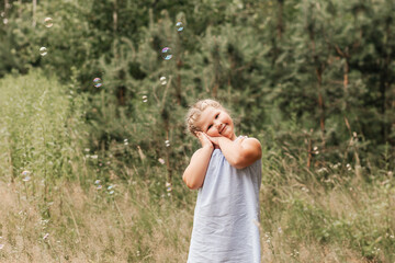 Obraz premium Little blond hair girl play with soap bubbles in park, family activity during summer. Feeling happiness, joyful, cheerful and enjoying. Playing in garden during sunbeam.