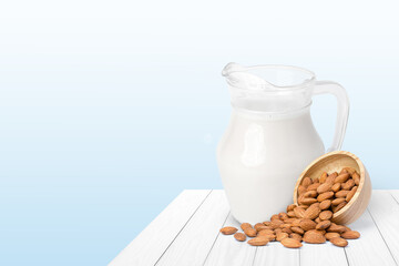 Glass of Almond milk and almond seeds in wooden bowl isolated on wood table with blue background. 