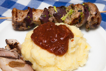 Mashed potatoes with tomato sauce and meat skewers on a white plate on the table.