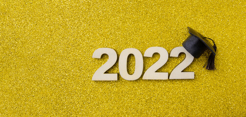 Graduated hat or cap with wooden number 2022 on a yellow glitter background. Class 2022 concept...