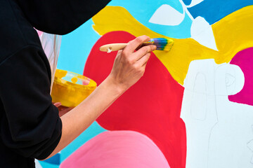 Artist in black hoodie painting colorful picture with paintbrush on white canvas at art festival