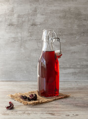 Red tea in a clear bottle on a canvas napkin. Dried hibiscus flowers on the table. Light wooden...