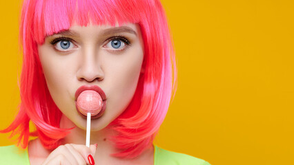 Freaky hipster woman in pink wig eat lick lollipop on bright yellow background
