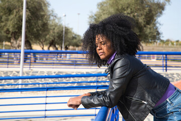 Fototapeta na wymiar Young and beautiful Afro-American woman is leaning on a blue railing. The woman looks at infinity. Concept of various expressions. Sadness, depression.