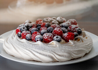 meringue cake with blueberries and raspberries on a plate on green background