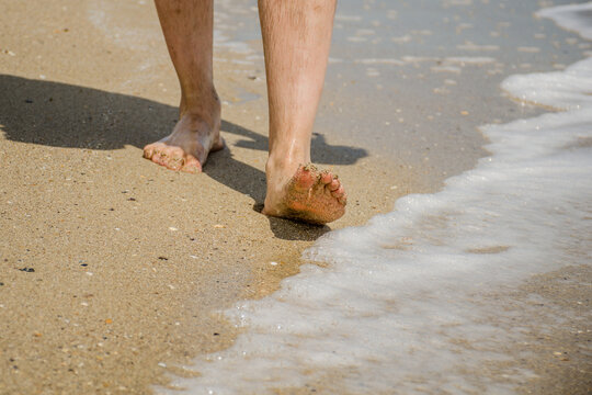 Men's feet go along the sandy seashore. Healthy lifestyle concept