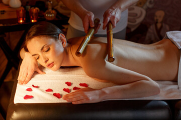 Relaxed girl having a massage with a bamboo stick in a beautiful dark salon. in a romantic relaxing setting
