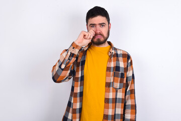Unhappy young caucasian man wearing plaid shirt over white background crying while posing at camera...