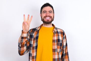 Naklejka premium young caucasian man wearing plaid shirt over white background showing and pointing up with fingers number three while smiling confident and happy.