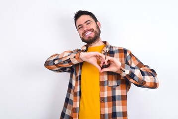 young caucasian man wearing plaid shirt over white background smiling in love showing heart symbol...