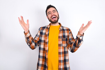 Fototapeta premium Cheerful young caucasian man wearing plaid shirt over white background making a welcome gesture raising arms over head.