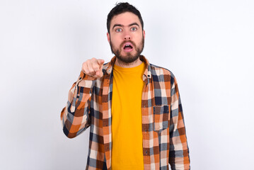 Shocked young caucasian man wearing plaid shirt over white background points front with index...