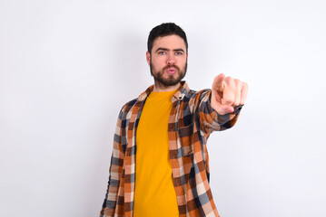 Cheerful young caucasian man wearing plaid shirt over white background indicates happily at you, chooses to compete, has positive expression, makes choice.