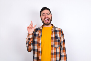 Fototapeta premium Pleasant looking young caucasian man wearing plaid shirt over white background has clever expression, raises one finger, remembers himself not to forget tell important thing.