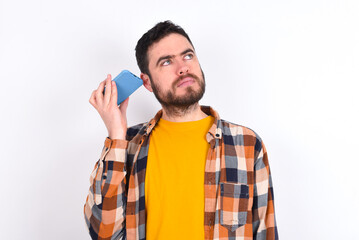 Smiling young caucasian man wearing plaid shirt over white background listening a voice message...