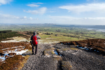 Male tourist with red backpack on a footpath in a mountains. County Sligo, Ireland. Cold winter season. Outdoor sport and activity. Travel and sport concept. Beautiful Irish nature in the background