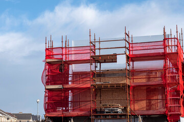 Fototapeta na wymiar Old home or office building construction with scaffolding and red mesh, blue sky in the background. White background. New house development. Construction industry. Repair work.