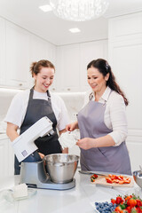 mother and daughter prepare cream or glaze in the mixer to decorate the dessert.