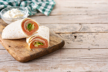 Salmon wrap sandwich roll with cheese and vegetables on wooden table. Copy space